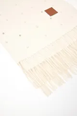 Pashmina color blanco roto con flecos en los extremos y decorada con perlas pequeñas. Incluye un parche de cuero sintético marrón con un logo grabado.