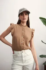 Camisa color marrón claro con textura arrugada, cuello mao con volados, mangas cortas con volados y cierre frontal con botones.