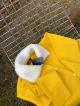 Cárdigan amarillo tejido en lana con cuello de piel sintética blanca y botones dorados.