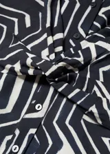 Vestido corto con estampado geométrico en blanco y negro, con cuello en V, mangas cortas y nudo en la cintura.