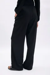 Pantalón negro de tiro alto con cintura elástica y corte ancho (wide leg). Presenta una textura sutil en la tela y bolsillos laterales.