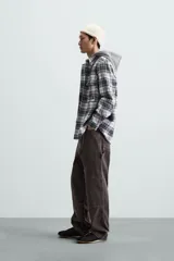 Sobrecamisa de hombre a cuadros azul marino y blanco, corte relaxed fit, con capucha gris de algodón, cuello solapa, manga larga con puños abotonados, bolsillos de parche en el pecho y bolsillos laterales en la cadera.