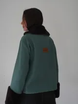 Campera corta negra con cuello y puños de piel sintética negra. Cierre con presillas de madera.