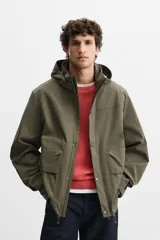 Parka verde militar confeccionada en tejido técnico ligero resistente al viento, con cuello alto, capucha, manga larga con puños ajustables, bolsillos de plastrón con solapa en la cadera, bolsillo interior, bajo ajustable con elásticos y cierre frontal con cremallera oculta por solapa con botones a presión.