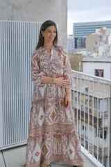 Vestido largo color rosa con estampado floral y geométrico en tonos blanco y naranja. Tiene cuello mao, mangas 3/4 y corte escalonado en la falda.