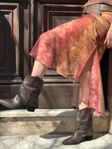 Bota corta de cuero sintético color marrón, con taco cuadrado y punta fina. Presenta una correa con tachas pequeñas y una argolla metálica decorativa alrededor del tobillo. Cuenta con cierre lateral.