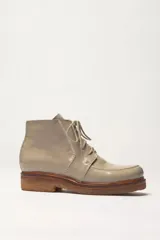 Bota corta de cuero vacuno con acabado charol color gris claro, estilo chukka o desert boot, con cordones beige y suela de goma color caramelo. Presenta costuras visibles en contraste y punta redondeada.