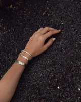 Pulsera tipo esclava abierta, con acabado rústico y textura irregular, en tono plateado. Se vende por unidad.