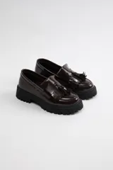 Mocasín marrón con detalles de flecos y suela gruesa.
