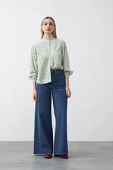 Camisa de viscosa blanca con estampa de lunares negros. Presenta cuello alto con volado y botonadura frontal, mangas largas con puños abullonados y frunces bajo el busto.