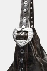 Bolso de hombro tipo shopper, color marrón oscuro con efecto envejecido o desgastado. Presenta un asa de hombro con detalle de tachas metálicas y ajuste mediante hebilla. El cierre principal es magnético e incluye un bolsillo interior con cremallera.