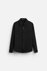 Sobrecamisa negra de tejido con elasticidad, cuello solapa y manga larga acabada en puño con botón a presión. Tiene bolsillos de plastrón en el pecho y cierre frontal con botones a presión.