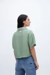 Blusa verde con escote en V, cuello camisero, manga corta y dos bolsillos en el pecho.
