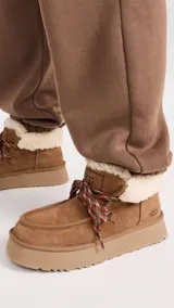 Botines UGG color marrón claro, con interior de piel sintética color crema, cordones de tela con diseño geométrico en marrón, rojo y blanco, y suela de goma color beige.