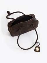 Cartera rectangular de estructura firme confeccionada en cuero descarne vacuno color marrón. Presenta manijas fijas, cierre superior y un charm metálico dorado en forma de vaquita de San Antonio colgando de un tag lateral. Incluye el logo de la marca grabado en relieve en el frente.