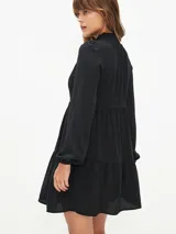 Vestido corto negro con cuello alto, mangas largas abullonadas y falda escalonada.