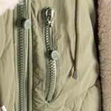 Campera verde con capucha, cierre frontal y tres bolsillos. Tiene puños ajustados y forro interno de poliéster.