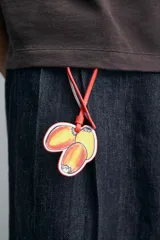 Llavero de cuero con diseño de tres frutas: dos mitades de durazno y una ciruela, con cordón de cuero naranja para colgar. Accesorio de la colección Filipe Jardim x Zara.