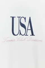 Sudadera blanca de algodón con cuello redondo, manga larga y texto bordado en azul marino en el frente que dice 'USA' y 'Tennis Club Division'.