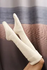 Medias largas tejidas a máquina en punto elástico hasta la rodilla, color crema.