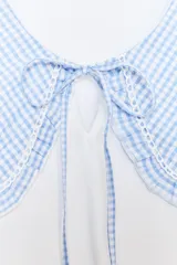Camiseta blanca de manga corta con cuello bobo de tela a cuadros vichy celeste y blanco con bordes bordados. El cuello tiene lazos finos del mismo tejido.