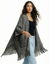 Kimono tejido en punto suave, color beige y crudo, con diseño de espiga (herringbone). Presenta mangas amplias, bolsillos frontales y terminación con flecos en el ruedo.