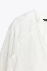 Camisa blanca de cuello redondo con escote en V y mangas largas acampanadas con volantes.