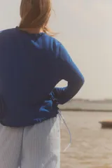 Chaqueta azul de punto con manga larga, volantes en el escote y en los puños, y cierre frontal con lazada.