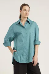 Camisa blanca de corte clásico con cuello abotonado, cierre frontal con botones y mangas largas con puños abotonados. Presenta pequeños apliques de strass plateados dispersos por toda la prenda.