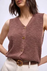 Chaleco de tejido de punto color crudo, sin mangas, con escote en V y cierre frontal de botones marrones.