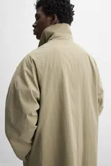 Gabardina color beige de corte amplio, con cuello solapa, manga larga, bolsillos laterales con solapa y cierre frontal con botones.