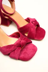 Sandalia de terciopelo verde con taco cuadrado de 7 cm, punta cuadrada y tiras anchas anudadas en el empeine. Cuenta con una tira fina ajustable al tobillo con hebilla dorada.