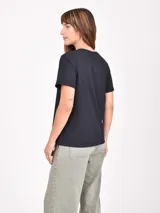 Remera blanca de manga corta con cuello redondo y un estampado artístico en tonos rojo oscuro y negro que simula una figura femenina con pantalón ancho a rayas.