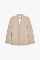 Blazer color beige, sin solapa, de manga larga con bolsillos de vivo en el delantero y cierre frontal con gancho metálico.