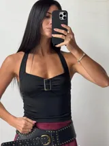 Top negro con breteles finos y escote halter. Presenta un aplique metálico rectangular en el centro del busto.