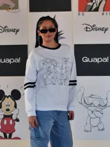 Buzo blanco de manga larga con cuello redondo y puños y ruedo en rib negro. Presenta un gran estampado frontal de la letra 'M' rellena de dibujos de personajes de Disney, incluyendo a Mickey Mouse. Las mangas tienen dos franjas negras a la altura del bíceps.