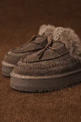 Slippers UGG de cuero color marrón con interior de piel sintética blanca, plataforma color marrón y cordones decorativos.