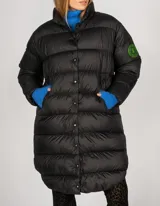 Campera puffer larga color beige, con cuello alto y cierre frontal con botones a presión. Tiene bolsillos laterales y un parche con el logo de la marca en la manga izquierda.