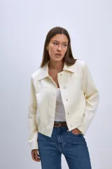Chaqueta color crema con cuello camisero, cierre frontal con botones a presión, bolsillos de parche en el pecho y corte cropped.