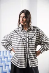 Camisa color crudo a rayas, de corte oversized con hombros caídos y silueta amplia. Presenta un recorte delantero con vivo contrastante, botones al frente y logo bordado al frente.