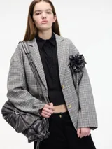 Blazer gris a cuadros con solapas de muesca, cierre con dos botones y corte holgado. Incluye un prendedor de flor negra en la solapa.