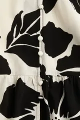 Vestido corto tipo túnica color blanco con estampado de flores negras, cuello mao, mangas cortas con doblez, botones frontales y falda con vuelo. Corte holgado.