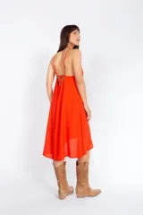 Vestido corto color naranja, con escote halter y diseño asimétrico con capas. Espalda con tiras regulables.