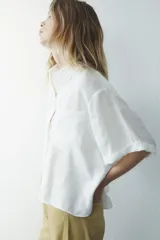 Camisa azul de cuello solapa y manga corta con dobladillo. Tiene dos bolsillos de parche en el pecho, bajo asimétrico con aberturas laterales y cierre frontal con botones ocultos.
