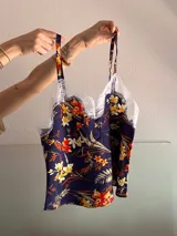 Top de fibrana con estampado floral en tonos naranja, amarillo y blanco sobre fondo azul marino. Presenta breteles finos regulables y detalle de encaje blanco en el escote.