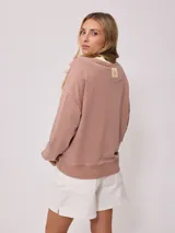 Sweater color ladrillo con cuello redondo en color crema. Estampado frontal con el texto 'Malibu Rusty' y un logo con forma de flor. Corte holgado.