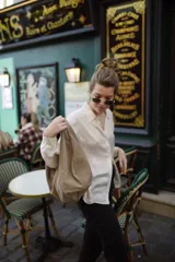 Bolso tipo hobo de cuero color beige, con asa anudada al hombro y cierre superior con cremallera.