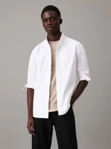 Camisa blanca de corte regular, confeccionada en tejido oxford de algodón y elastano. Tiene mangas largas con puños abotonados, cierre frontal con botones y cuello clásico. Incluye etiqueta con el logo de Calvin Klein.