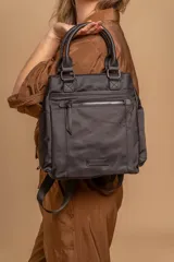 Mochila bandolera color marrón con herrajes color peltre. Tiene un compartimento principal amplio con cierre, un bolsillo frontal con cierre y dos bolsillos laterales abiertos. Incluye correa ajustable para usar al hombro o cruzada.