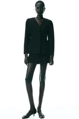 Blazer negra entallada, de escote pico y manga larga con hombreras. Tiene bolsillos delanteros de vivo y cierre frontal con botones a presión ocultos.